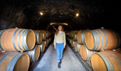 A woman explores a dimly lit wine cellar tunnel, walking between rows of wooden barrels on an exclusive Classic Wine Tour.