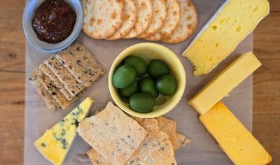 Gourmet cheese board featuring artisan crackers, three premium cheeses, green olives, and chutney—ideal for a wine tasting tour.