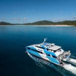 SeaLink’s iconic blue and white ferry sails past lush green hills, inviting you on a top-rated Purely Whitehaven Day Tour adventure.