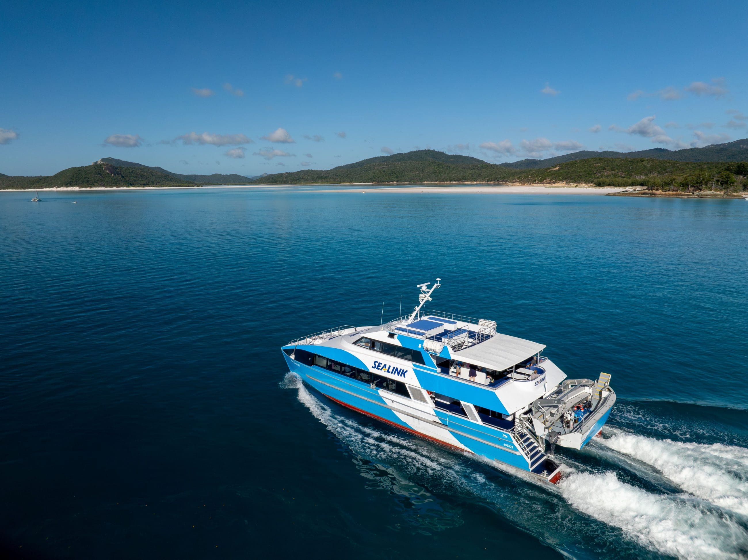 SeaLink’s iconic blue and white ferry sails past lush green hills, inviting you on a top-rated Purely Whitehaven Day Tour adventure.
