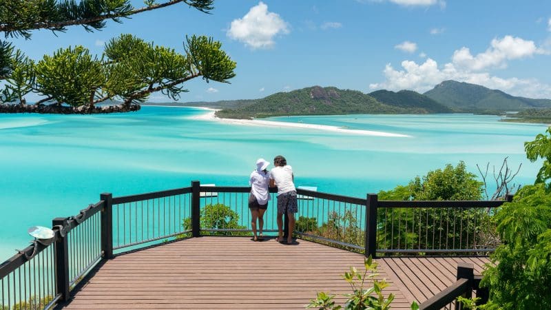 Couple enjoys stunning turquoise waters and scenic islands from a deck on a luxury Purely Whitehaven Day Tour in the Whitsundays.