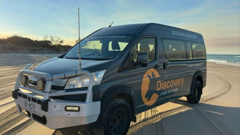 Discovery tour van on a sandy beach at sunset during K'gari 2 Day Tour, Noosa; stunning coastal view, ideal adventure destination.