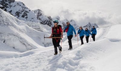 Five adventurers in winter gear trek across Franz Josef Glacier, framed by dramatic snow-capped peaks on a guided glacier hiking tour.