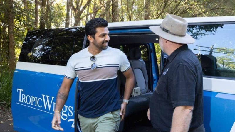 A traveller exits a Tropic Wings van, embarking on a Private Exclusive Atherton Tablelands Tour beneath clear, sunny skies.