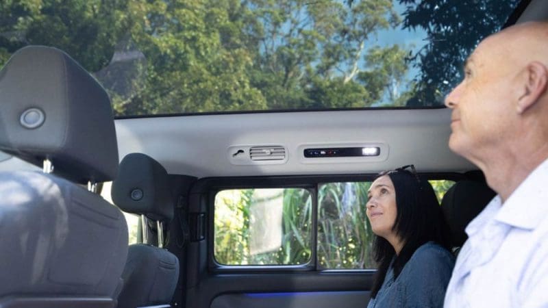 Experience a Private Exclusive Atherton Tablelands Tour: two guests admire lush treetops through a panoramic sunroof inside a luxury car.