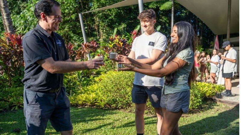 A man offers a mug to a smiling woman outdoors on a Private Exclusive Daintree Cape Tribulation Tour, enjoying tropical rainforest views.