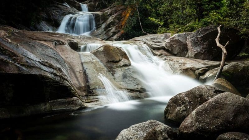 Stunning waterfall cascades over smooth rocks amid lush rainforest on a Private Exclusive Atherton Tablelands Tour in Queensland.