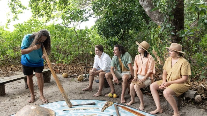 A man skilfully plays the didgeridoo for a small group outdoors, capturing highlights of the 16 Day Best of East Coast Australia Tour.