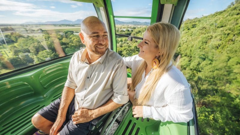Happy couple riding a cable car over vibrant green hills on the 16-Day Best of East Coast Australia Tour from Sydney, scenic views.