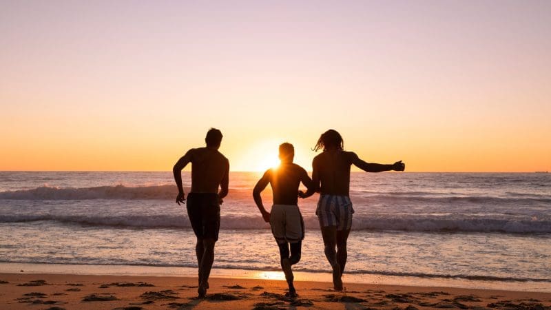 Three travellers run towards the sea at sunset during an epic 8 Day Sydney to Brisbane Fraser Island Comfort Tour adventure.
