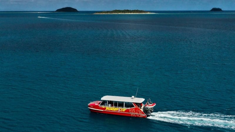 Vibrant red tour boat glides on clear blue ocean during 14 Day Sydney to Cairns Fraser Island Whitsundays Comfort Tour adventure.