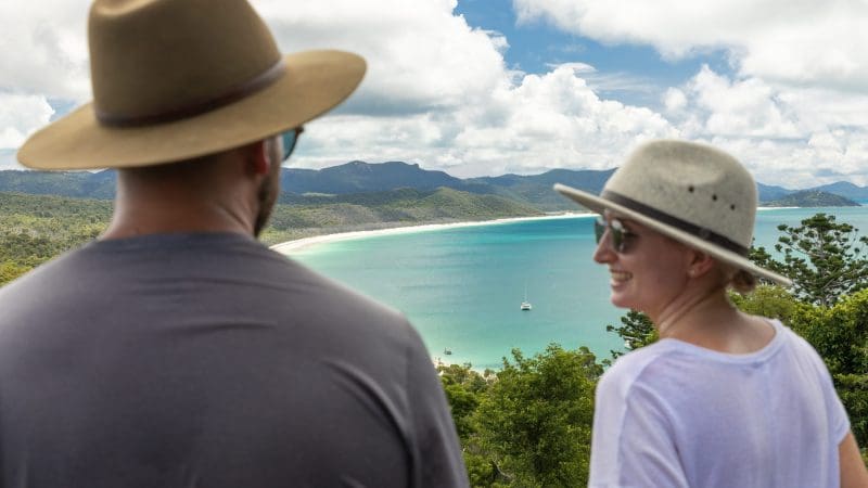 Two travellers in sun hats admire a breathtaking bay view—ideal for a 14 Day Sydney to Cairns with Fraser Island Whitsundays Comfort Tour.