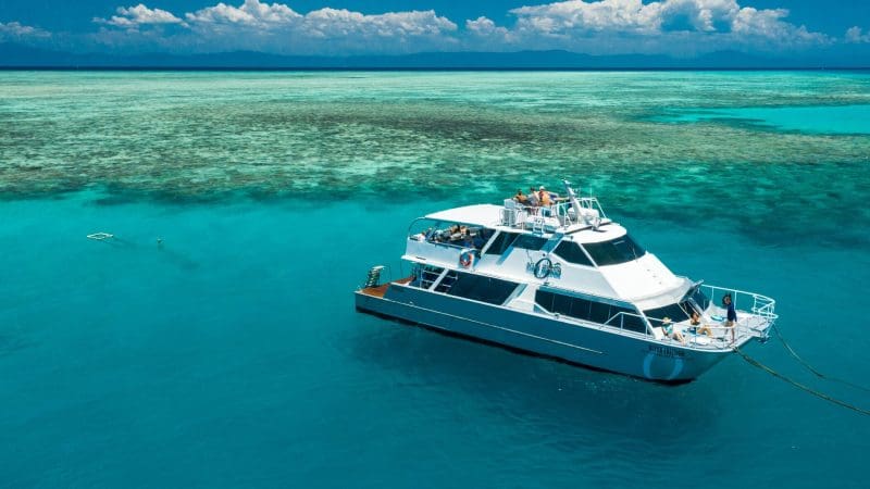 Luxurious white yacht anchored by a vibrant coral reef during the 14-Day Sydney to Cairns Fraser Island & Whitsundays Comfort Tour.