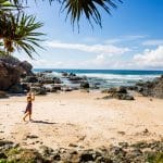 Traveller in a sunhat walks along a scenic rocky, sandy beach—highlight of the 16 Day Best of East Coast Australia Comfort Tour from Sydney.