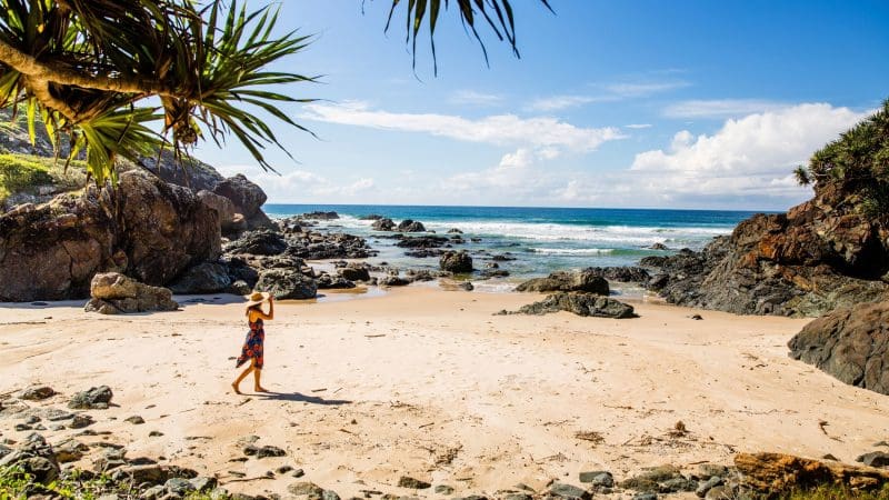 Traveller in a sunhat walks along a scenic rocky, sandy beach—highlight of the 16 Day Best of East Coast Australia Comfort Tour from Sydney.