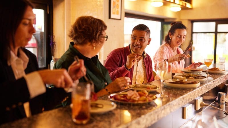 Four travellers relax at a stylish bar, sharing delicious food and lively stories from their 8 Day Sydney to Brisbane Fraser Island tour.