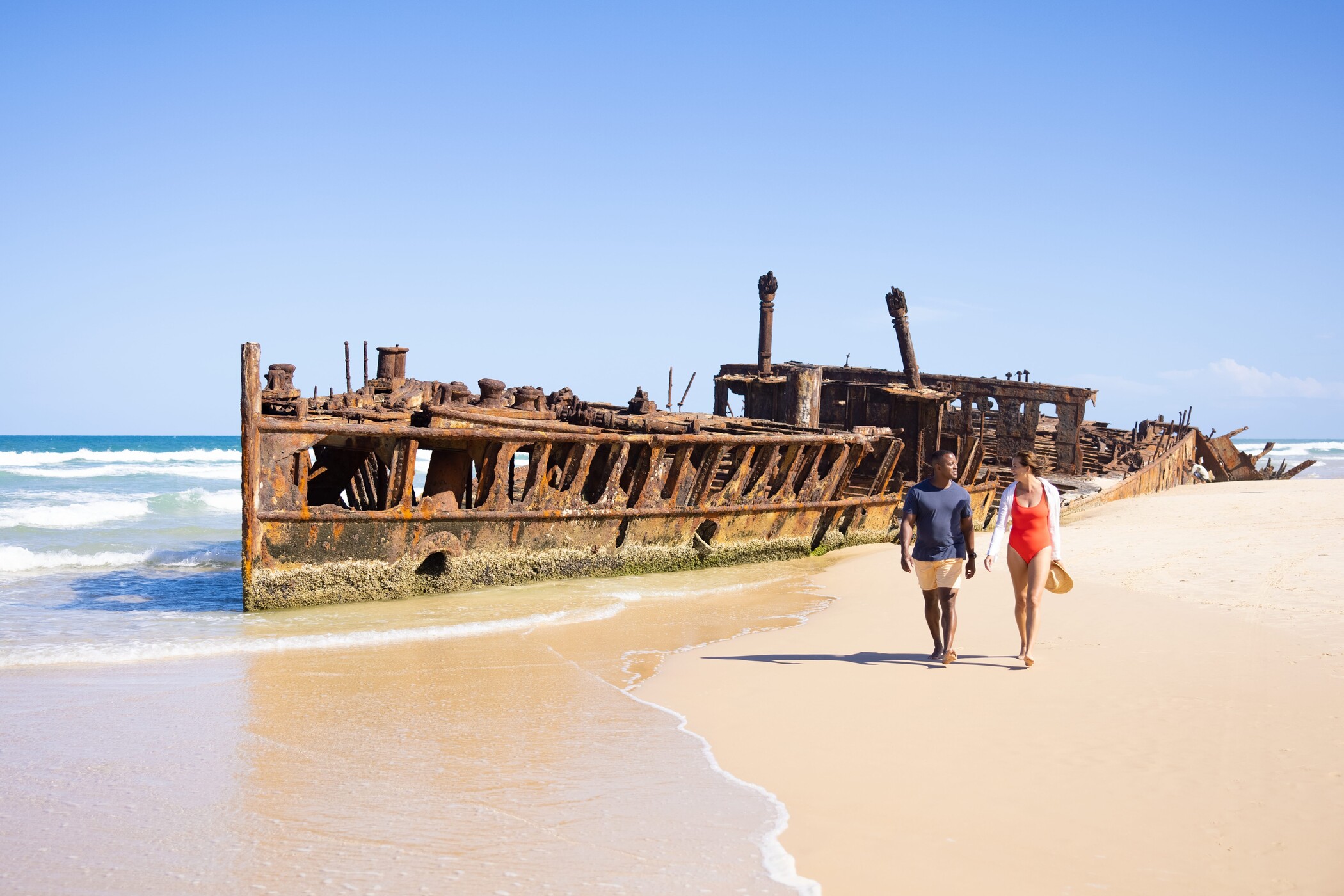 Couple walks by a rusty shipwreck during a 14-Day Sydney to Cairns tour with stops at Fraser Island and Whitsundays, Australia.