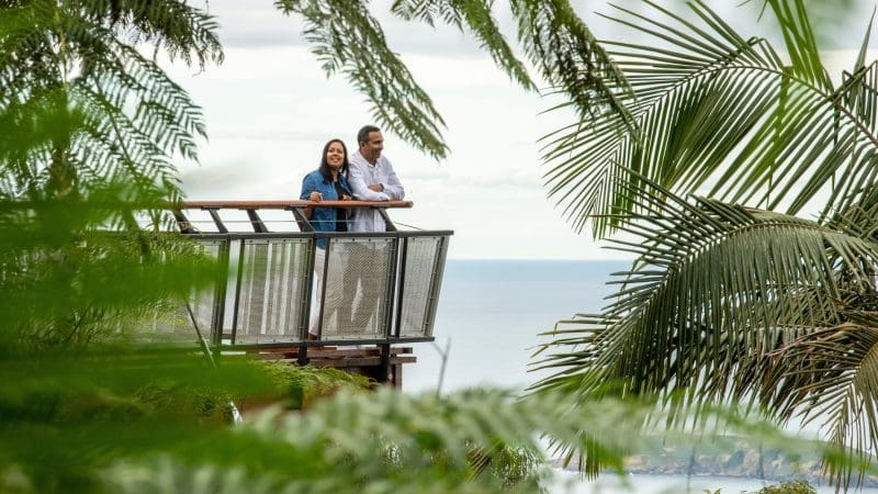 A happy couple enjoys panoramic ocean views and lush greenery from a balcony on the 16-Day Best of East Coast Australia Tour.