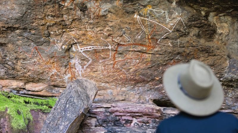 Traveller in a wide-brim hat admires ancient Aboriginal rock art during Kakadu Wilderness Escape and Crocodile Cruise adventure tour.