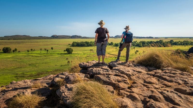 Two adventurers in wide-brimmed hats stand on rocky terrain, admiring Kakadu’s landscape during a 1 Day Wilderness Escape and Crocodile Cruise.