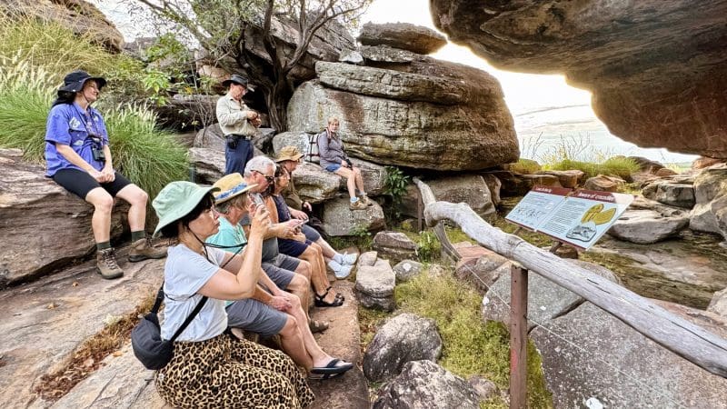 Visitors gather on rocks as an expert guide shares insights during the 1 Day Kakadu Wilderness Escape with Fogg Dam Wetlands tour.