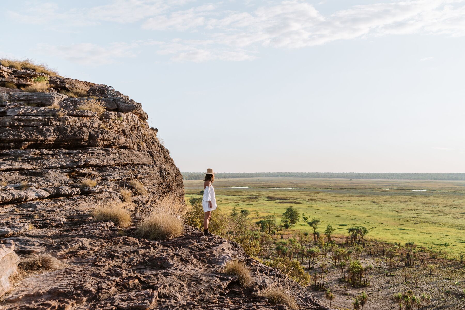 Traveller in white standing atop a rugged cliff, overlooking lush green plains—ideal for an unforgettable 1 Day Kakadu Wilderness tour.