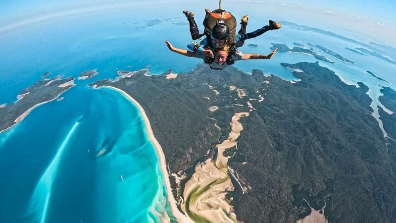 Experience an exhilarating tandem skydive over Whitehaven Beach, captured on video and photos, above turquoise waters and lush islands.