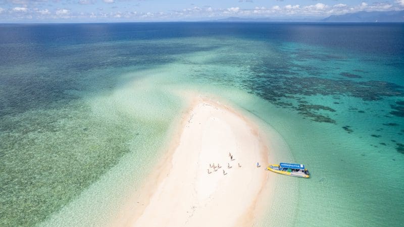 Discover a picturesque sandbank at Great Barrier Reef Eco Adventure, surrounded by crystal-clear blue waters, visitors, and a tour boat.