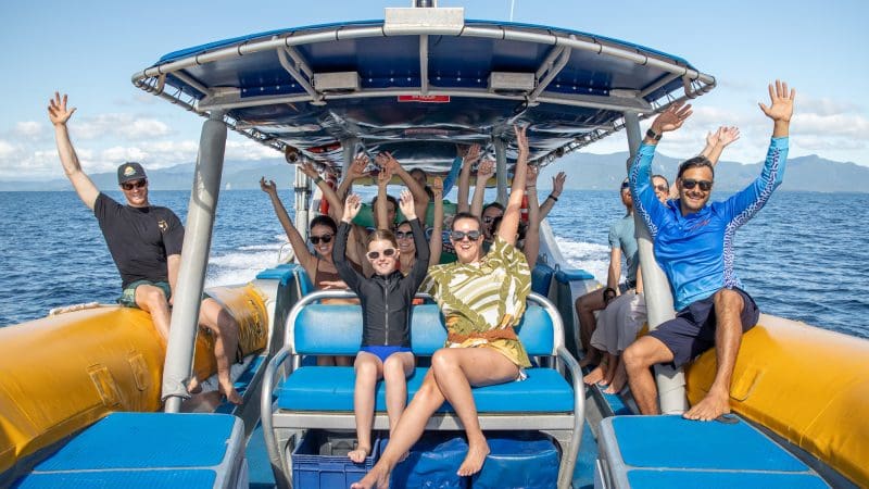 Smiling group with raised arms enjoys a thrilling Great Barrier Reef Eco Adventure cruise on sparkling blue water under bright sunshine.