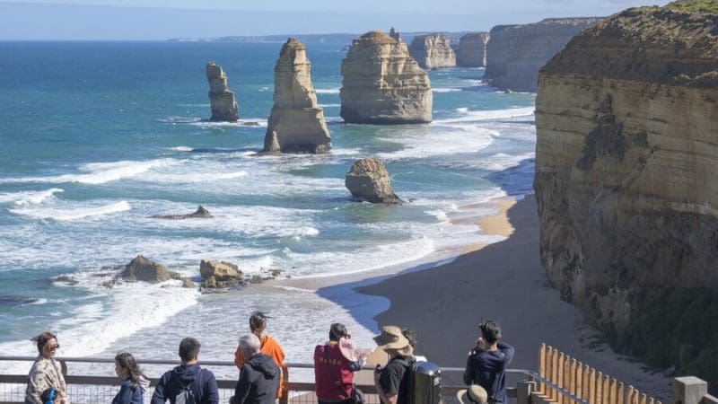 Tourists marvel at the iconic Twelve Apostles during a 1 Day Great Ocean Road Reverse Eco Tour, witnessing stunning coastline views.