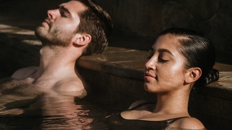Couple relaxing in a sunlit Peninsula Hot Springs pool, savouring their 1 Day Spa Entry with Shuttle Bus for the ultimate wellness escape.