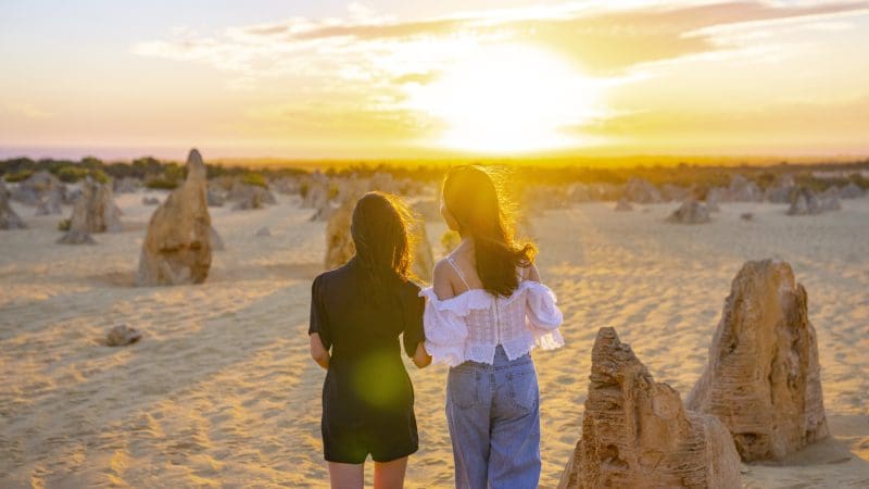 Experience the breathtaking 1 Day Pinnacles Sunset Stargazing Tour by Autopia as two travellers explore sandy desert dunes at sunset.
