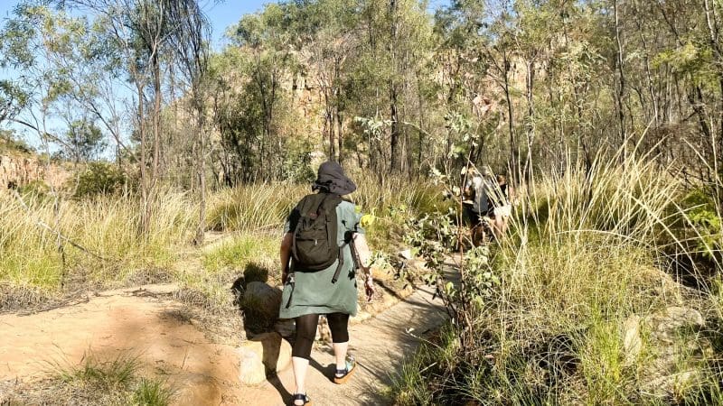 Traveller with a rucksack hikes along a vibrant, sunlit trail, evoking the adventure of a Katherine Gorge Cruise from Darwin.