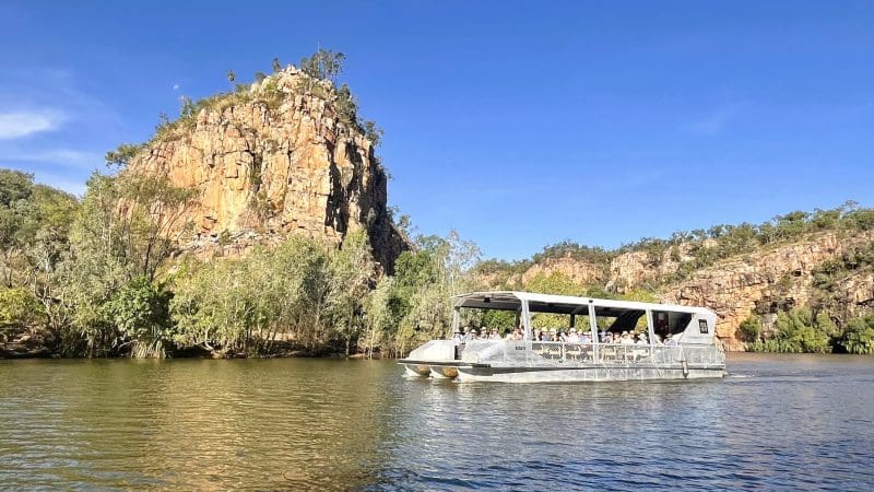 Experience a 1 Day Katherine Gorge Cruise gliding past dramatic rocky cliffs and lush trees beneath a clear blue sky—ideal from Darwin.