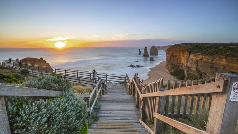 Wooden stairs descend to a golden beach at sunset on the 1 Day Great Ocean Road Sunset Tour from Melbourne, cliffs and sea view.