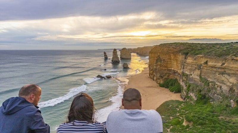 Travellers marvel at iconic limestone cliffs glowing at sunset during a 1 Day Great Ocean Road Sunset Tour from Melbourne.