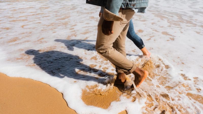 Experience two travellers with rolled-up trousers walking barefoot on the sand during a Great Ocean Road sunset tour from Melbourne.