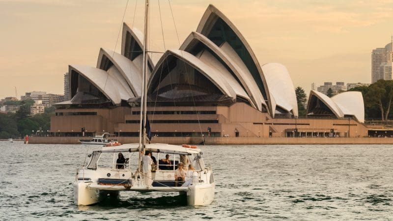 Experience a stunning BYO Sunset Sparkle Cruise on Sydney Harbour, with a catamaran sailing past the iconic Opera House at golden hour.