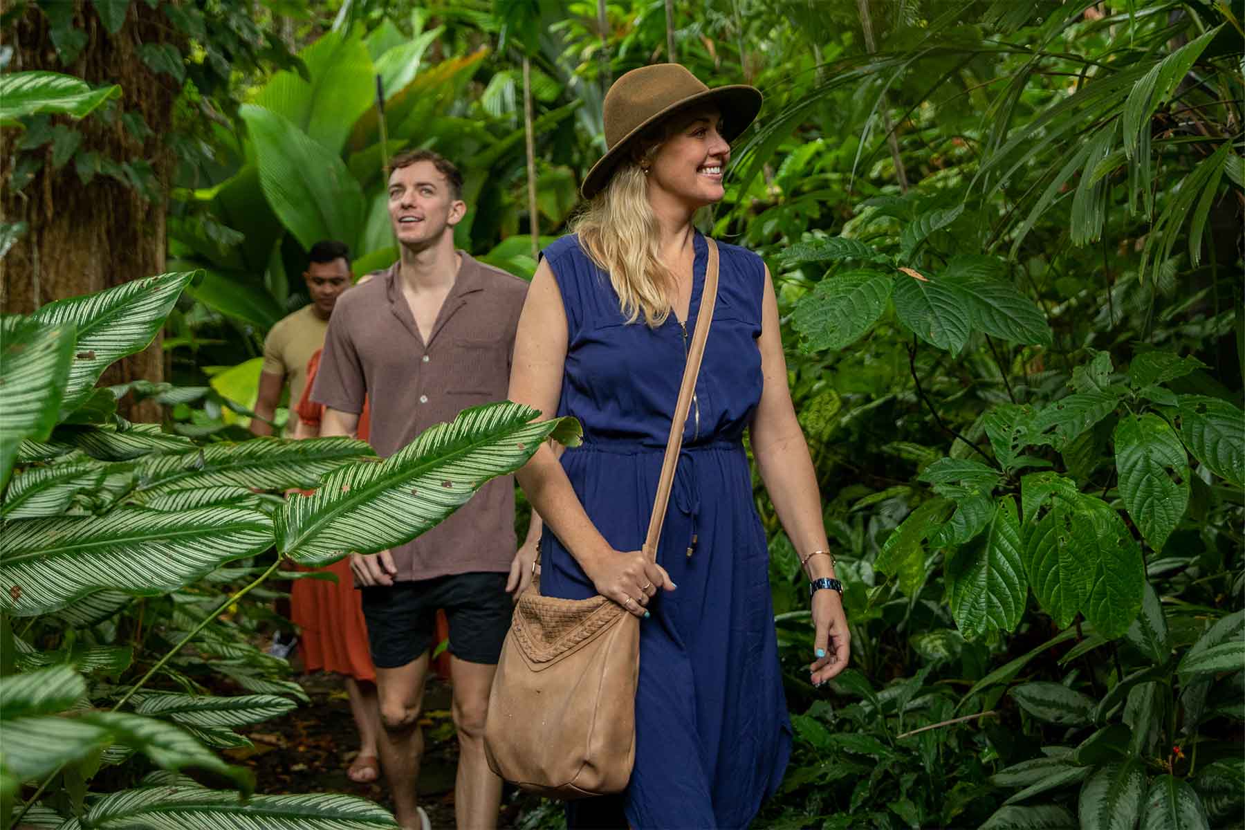 Two people smile as they walk among lush tropical plants on a CSHD Tour, with more following in Cairns City.