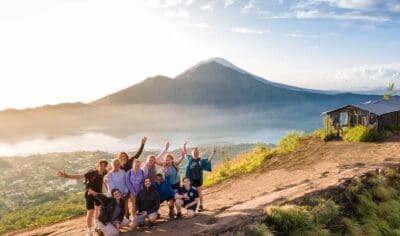 Happy group hiking a sunrise mountain trail in Indonesia, volcano and serene lake vistas in the background, tour adventure.